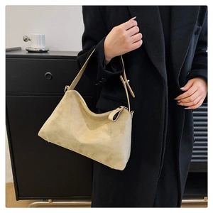 Détail du sac hobo en daim kaki avec bandoulière réglable sur un manteau noir élégant