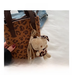 Detail of leopard print mini handbag with plush cat charm on white textile background