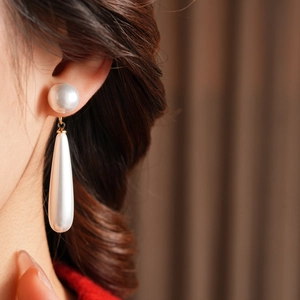 Macro shot of long drop-shaped pearl earrings with elegant golden metal hooks