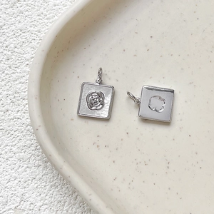 Macro shot of silver square charms with rose and clover patterns on ceramic plate