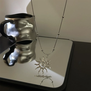 Macro shot of silver sun pendant with a textured chain reflected on a mirror