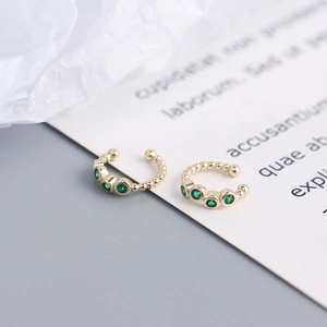 Macro shot of gold ear cuffs with green gemstones and beaded edges for non-pierced ears
