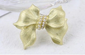 Macro shot of gold bow brooch featuring brushed metal texture and vertical pearl rows
