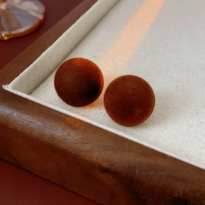 Detailed view of flocked ball earrings in deep brown matte velvet on light fabric