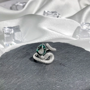 Detail of silver snake ring with green enamel and clear gemstone on dark stone base