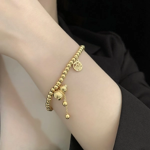 Close-up of golden beaded bracelet with Fu character and gourd charm on a model's wrist