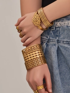Detailed view of bohemian gold leaf hollow bangles and carved rings on model wrist