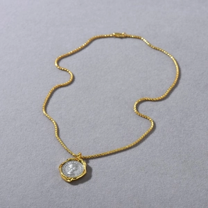 Macro detail of bimetal lucky coin necklace showing Elizabeth II relief on gold twist chain