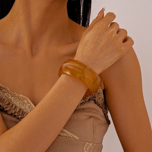 Close-up of a wide amber resin bangle with natural marble texture on a female model