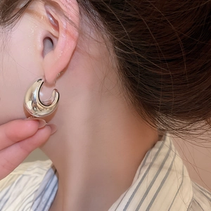 Close-up of a silver C-shaped acrylic hoop earring worn by a model with a glossy finish