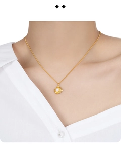Detail view of a gold S925 sterling silver necklace with a white pearl on a white shirt
