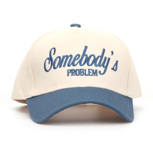 Detail of blue 'Somebody's PROBLEM' embroidery on two-tone canvas baseball cap