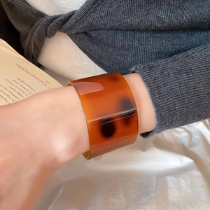 Close-up of a wide amber tortoiseshell resin cuff bracelet styled with knitwear
