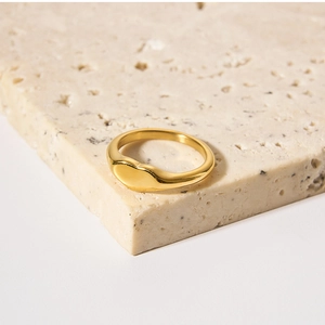 Detailed view of an 18K gold-plated heart signet ring on a beige travertine stone surface