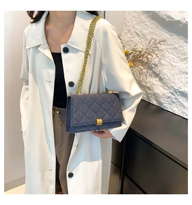 Detail of dark blue denim crossbody bag with gold chain and quilted pattern on a model