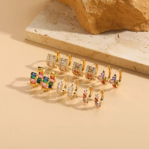 Detail of 6 pairs gold huggie earrings with colored zircons on stone background