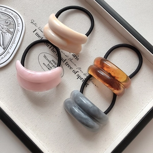 Detail of four acrylic hair rings with marble texture in cream, pink, amber, and grey