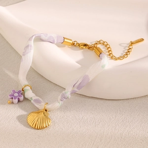 Detail of lavender floral ribbon bracelet with gold seashell pendant on a white tray