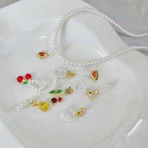 Close-up of pearl necklace with colorful fruit pendants and gold findings on a white plate