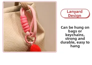 Close-up of pink braided lanyard with red plush ball keychain on a beige bag