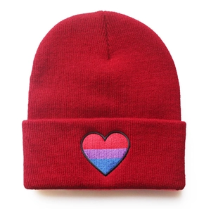 Close-up detailed view of a red knitted beanie with a bisexual pride heart embroidery.