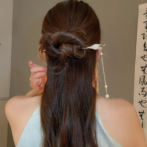 Détail d'un élégant pic à cheveux doré avec des pétales blancs et de longs glands perlés