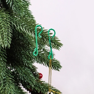 Close-up of green plastic S-shaped hooks hanging gold string on Christmas tree branches