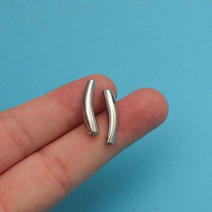 Close-up of small silver-colored curved metal tube beads for DIY jewelry on a finger