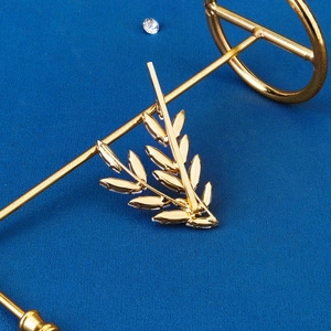 Close-up of golden leaf hair clip featuring marquise-cut rhinestones on blue background