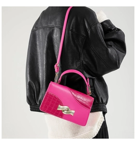 Detail of rose red croc-embossed handbag with wavy gold metal buckle on leather jacket