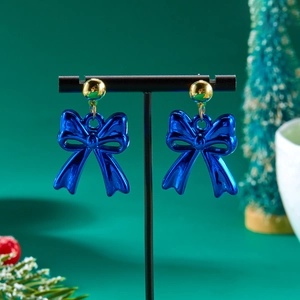 Colorful blue bow drop earrings with gold studs set against a festive Christmas background