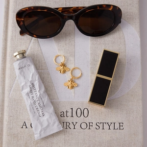 Golden bee charm earrings arranged with sunglasses and luxury accessories on a book