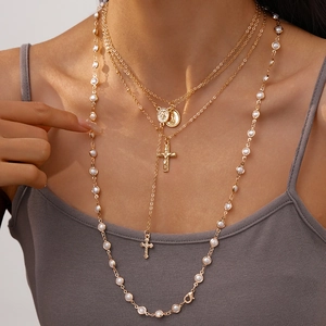 Detail of layered gold-tone necklace with faux pearl chain, cross and oval medal pendant