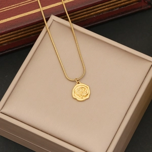 Detail of rose embossed gold coin pendant necklace on a beige jewelry gift box
