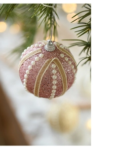 Pink glitter Christmas ball with white pearls and rope detail on a green pine branch