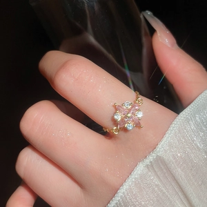Nahaufnahme von Goldkettenring mit rosa Zirkonia-Blume an der Hand vor dunklem Hintergrund