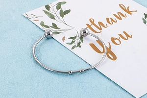 Detailed view of a silver stainless steel open bangle with bead ends on a card