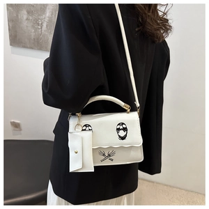 Detail view of white leather shoulder bag with punk skull print and small side pouch attachment