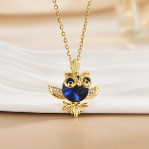 Golden owl pendant necklace with a large blue gem and sparkling crystal micro-pave details