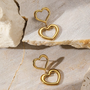 Close-up of golden double heart drop earrings on a natural stone background