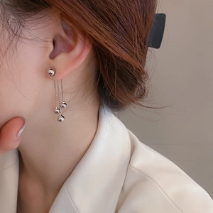 Detail view of silver bead tassel earrings featuring a three-chain drop design on a model