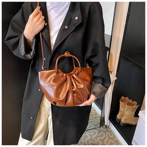 Detail shot of a brown ruched cloud bag with glossy faux leather texture and handles