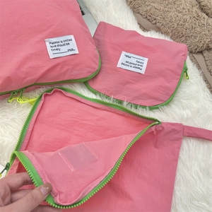 Detail view of pink nylon travel organizers with neon green zippers on white plush rug