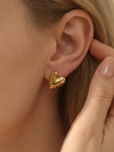 Detail of golden heart stud earrings featuring unique hammered texture on the earlobe