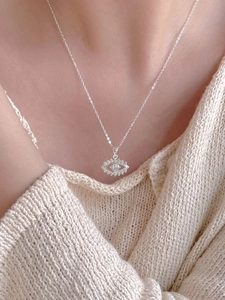 Detail of silver evil eye necklace with zircon stones worn on a beige knit sweater