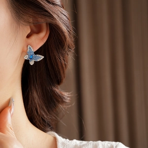 Primer plano de aretes de mariposa con piedra azul en forma de gota y cristales finos