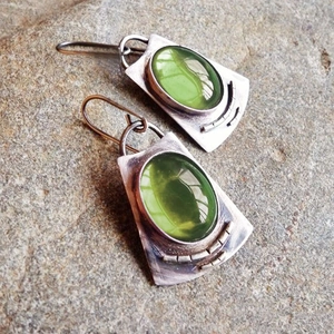Pendientes de plata vintage con piedras verdes ovales sobre fondo de roca natural