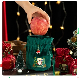 Detail of hand placing an apple into a green velvet Christmas gift bag with a gold bell