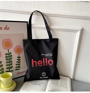 Detail shot of black Oxford fabric tote bag with printed red lettering on a desk