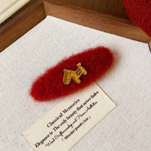 Détail d'une barrette en velours rouge avec un cheval doré sur un fond en tissu neutre